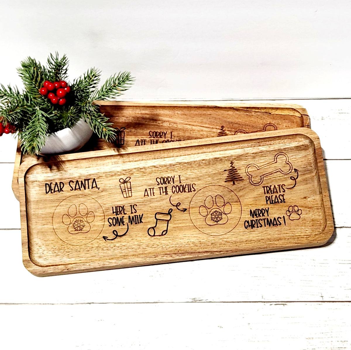 Engraved acacia wood Santa Paws treat tray reading Dear Santa Here Is Some Milk Sorry I Ate The Cookies Treats Please Merry Christmas with paw print and bone graphics, styled on a white wood surface with holiday greenery and red berries