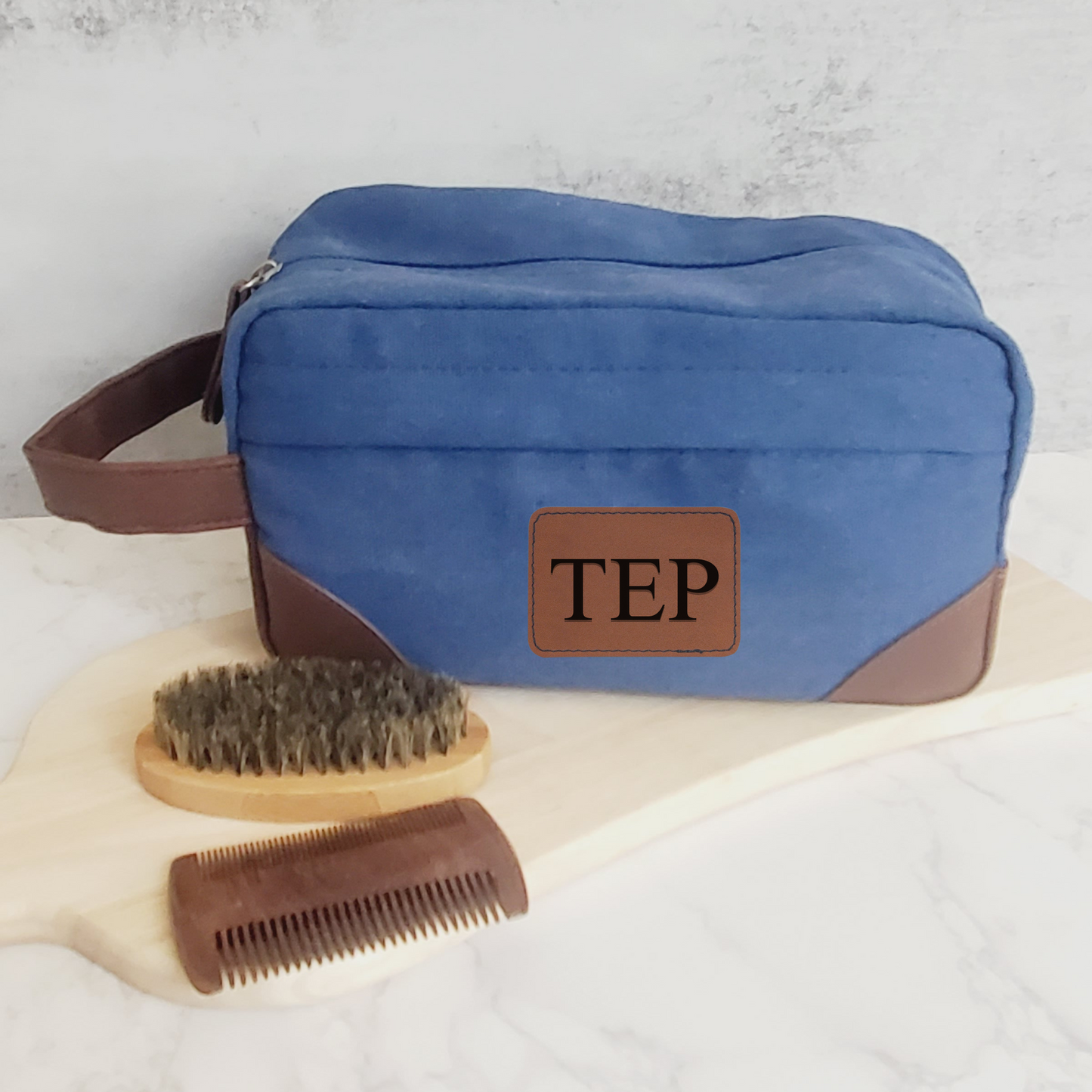 Blue men's toiletry bag with brown leather accents and handle.  Engraved with 3 initials on brown leather patch.