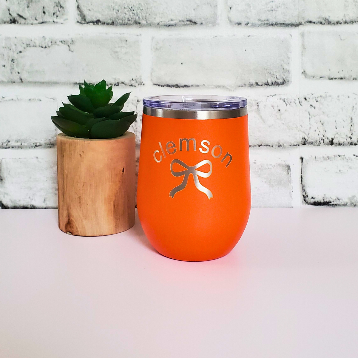Orange wine tumbler with 'Clemson' and a bow design on a white brick background