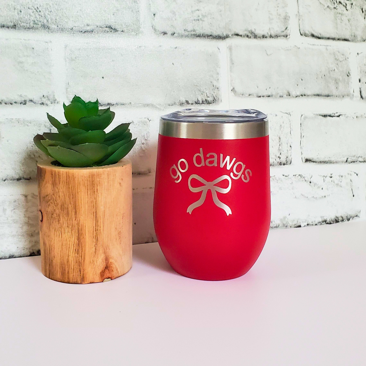 Red wine tumbler with 'go dawgs' design next to a small potted plant on a white surface.