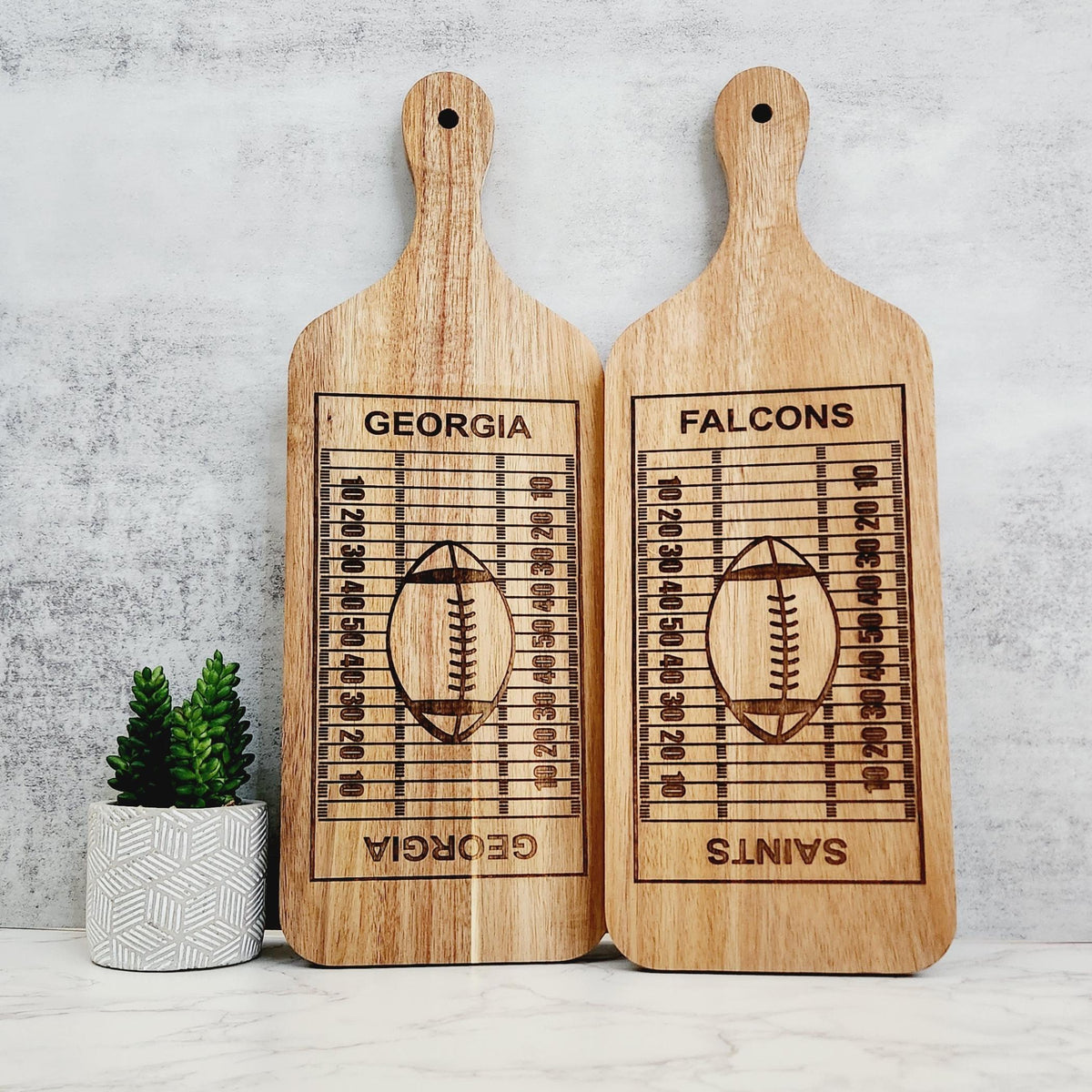 2 Wooden cutting boards with football fields engraved on them.  One board has Georgia in the football field end zones.  Another board has Falcons and Saints in the end zones.