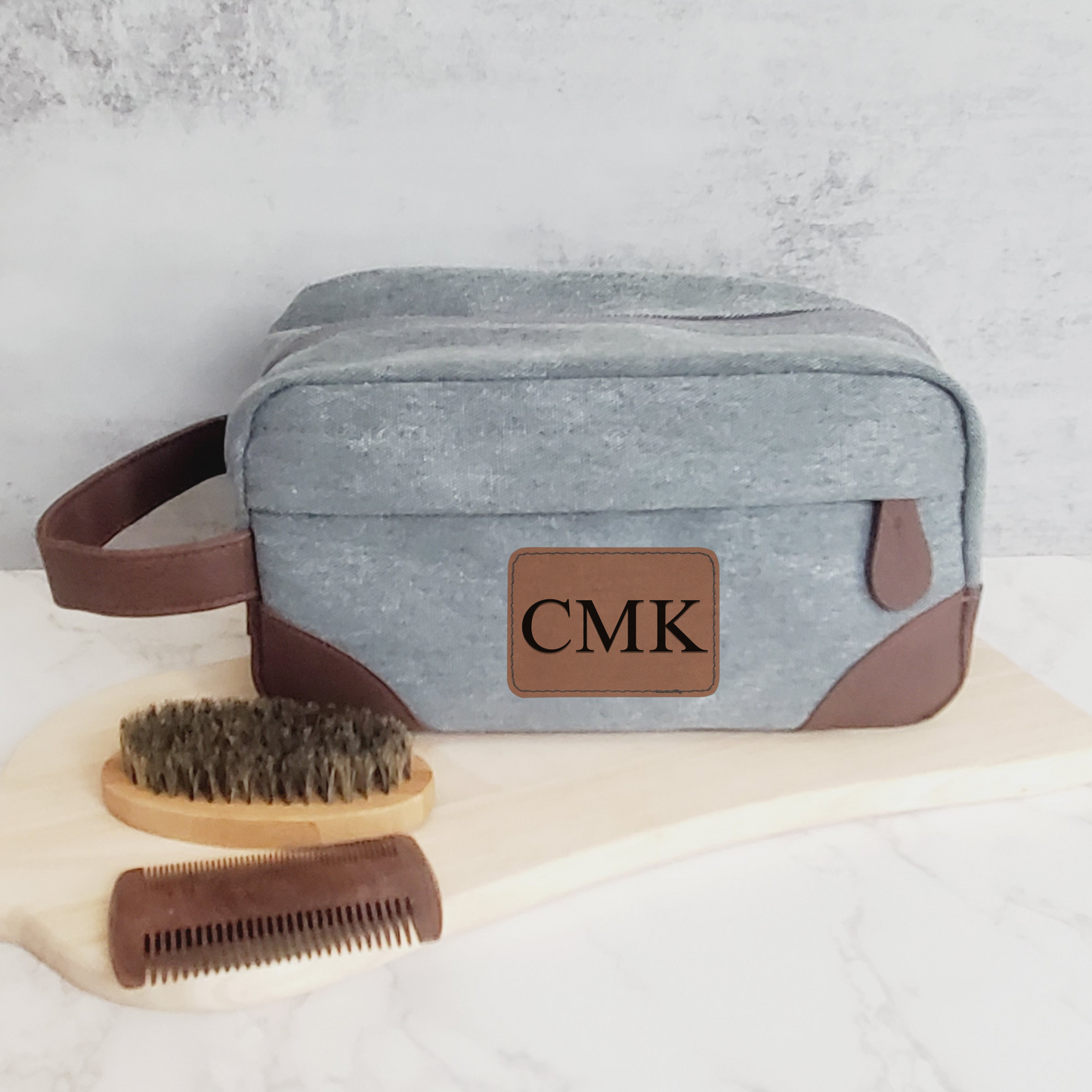 Gray men's toiletry bag with brown leather accents and handle.  Engraved with 3 initials on brown leather patch.