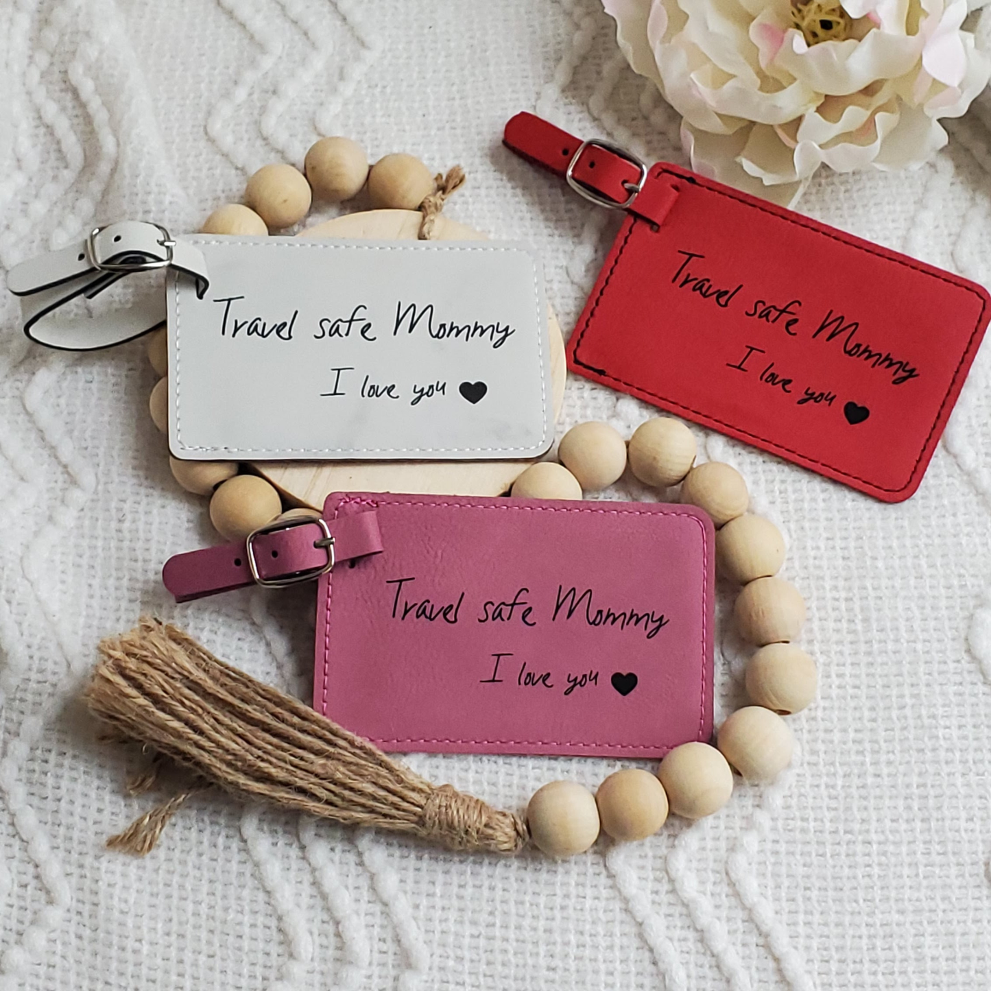 Group of luggage tags colored red, white, and pink with the words Travel safe Mommy I love you and a heart engraved in black.