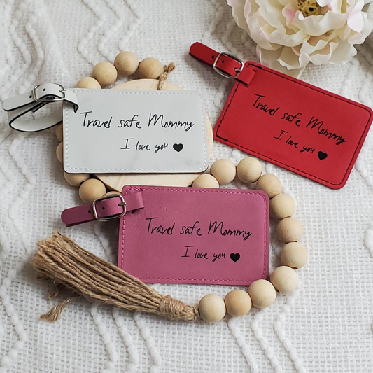 Group of luggage tags colored red, white, and pink with the words Travel safe Mommy I love you and a heart engraved in black.
