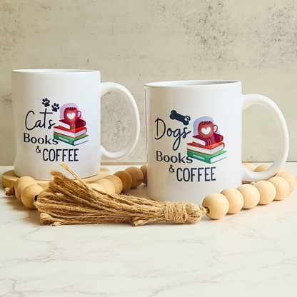 Two white ceramic mugs with 'Cats Books & COFFEE' and 'Dogs Books & COFFEE' prints, styled with wooden beads and a jute tassel on a marble surface against a textured beige wall.