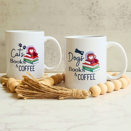 Two white ceramic mugs with 'Cats Books & COFFEE' and 'Dogs Books & COFFEE' prints, styled with wooden beads and a jute tassel on a marble surface against a textured beige wall.
