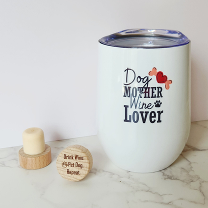 White 12 oz Dog Mother Wine Lover insulated stainless steel tumbler with paw print graphic, shown with two engraved wooden wine cork stoppers on a marble surface