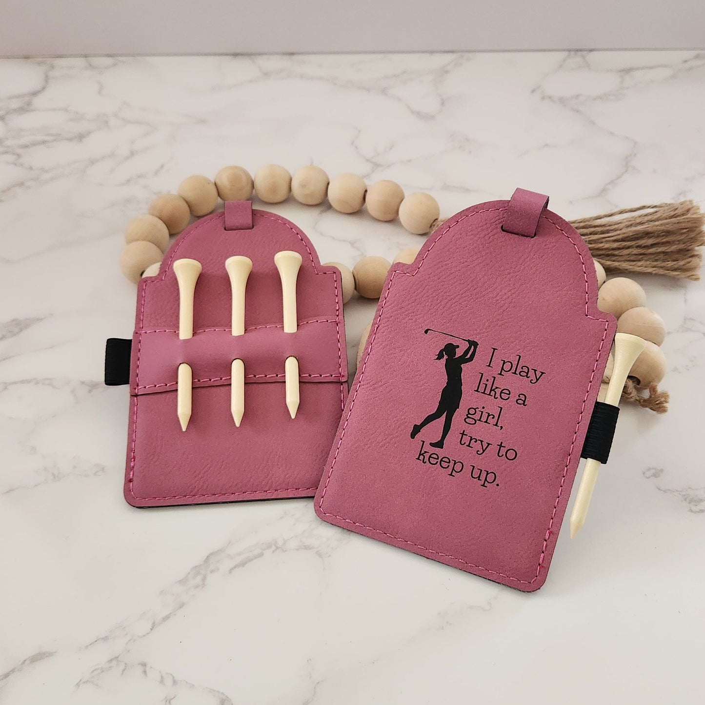 Pink Golf Tag engraved with lady swinging a golf club silhouette and the words " I play like a girl, try to keep up."  The back of the golf tag has 3 wooden golf tees in a holder.