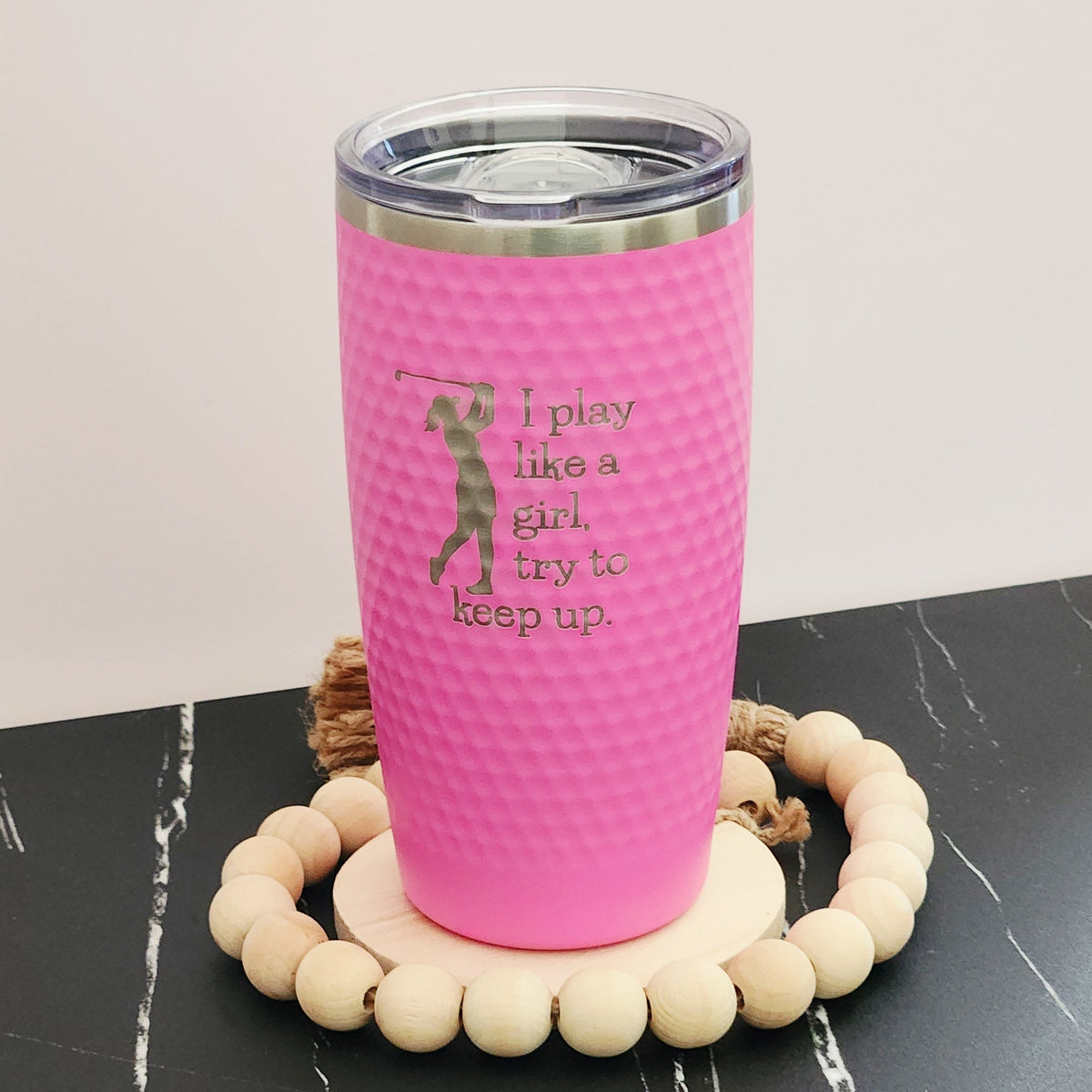 Pink dimpled golf tumbler with a golfer silhouette and silver engraving reading ‘I play like a girl, try to keep up".
