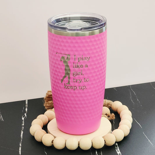 Pink dimpled golf tumbler with a golfer silhouette and silver engraving reading ‘I play like a girl, try to keep up".