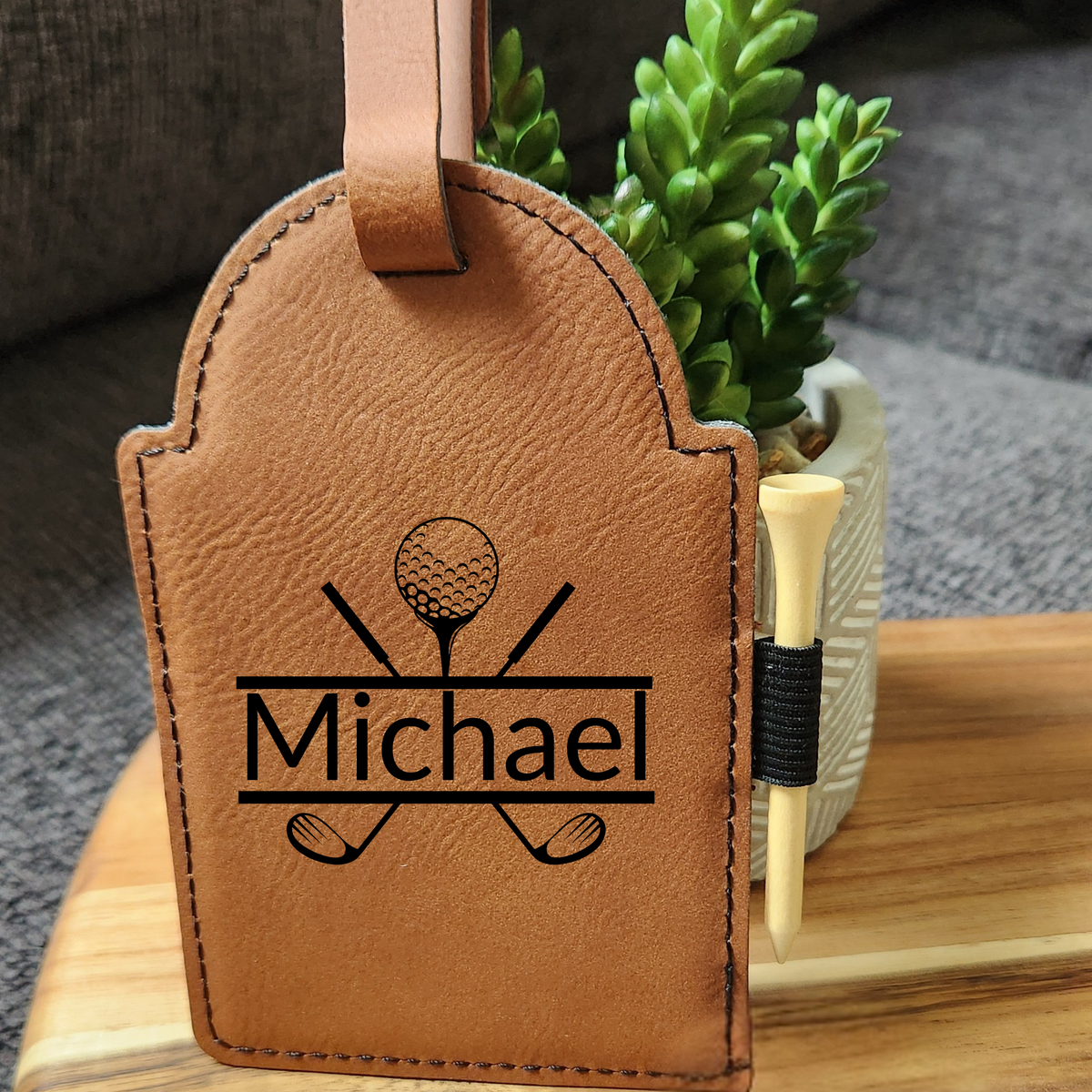 Tan vegan leather golf bag tag engraved with Michael and a golf design, with a wooden tee in the side loop.