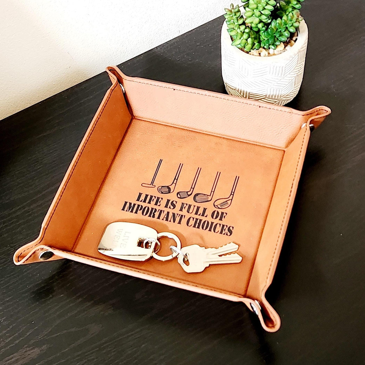 Tan vegan leather valet tray holding keys, with black golf club engraving and the message Life is full of important choices.